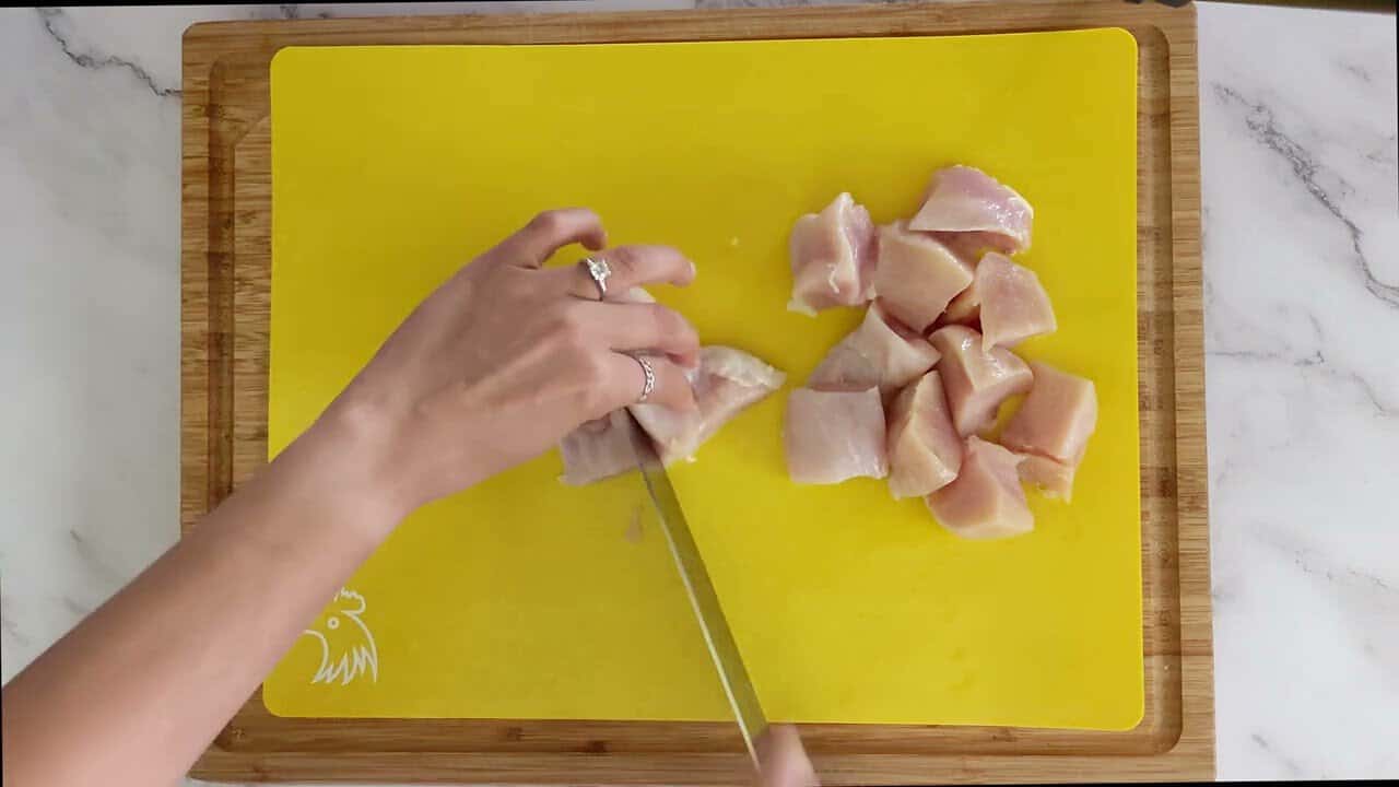 cutting chicken breast into large chunks on a cutting mat for raw poultry.